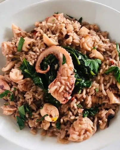 A bowl of seafood rice with octopus and greens
