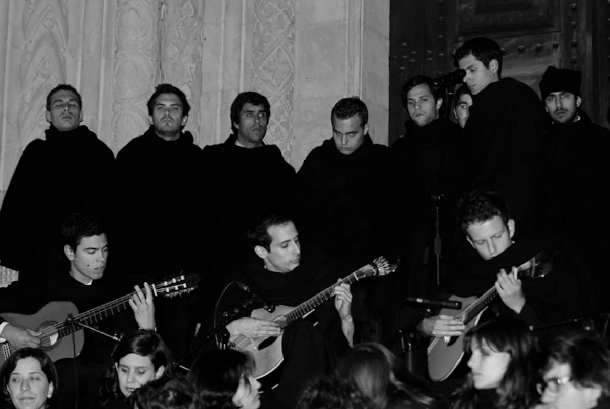A Coimbra fado singer in the black academic cape with two guitarists on a small stage