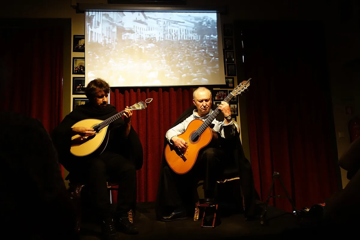Two musicians playing the teardrop-shaped Coimbra guitar at a fado concert