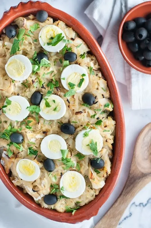 Salt cod baked with sliced egg and black olives in a terracotta dish