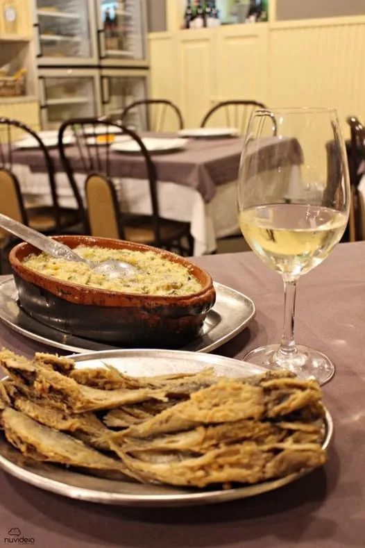 A clay pot dish and a plate of fried fish with white wine on a laid table